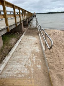 Foto av ramp med ledstång som går ner i vatttnet vid strand