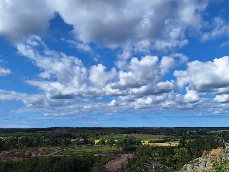 Foto visar himmel med vita moln och utsikt över skog och fält