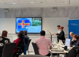 foto av personer som tiitar på presentation med skärm som visar Ålands flagga