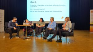 Foto av personer på rad på stolar framför skärm