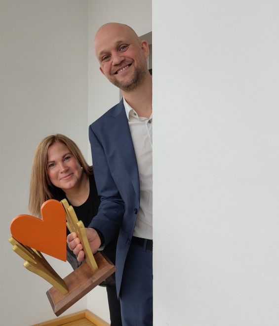 Foto visar två personer med ett pris i form av ett hjärta, som tittar fram bakom en vägg