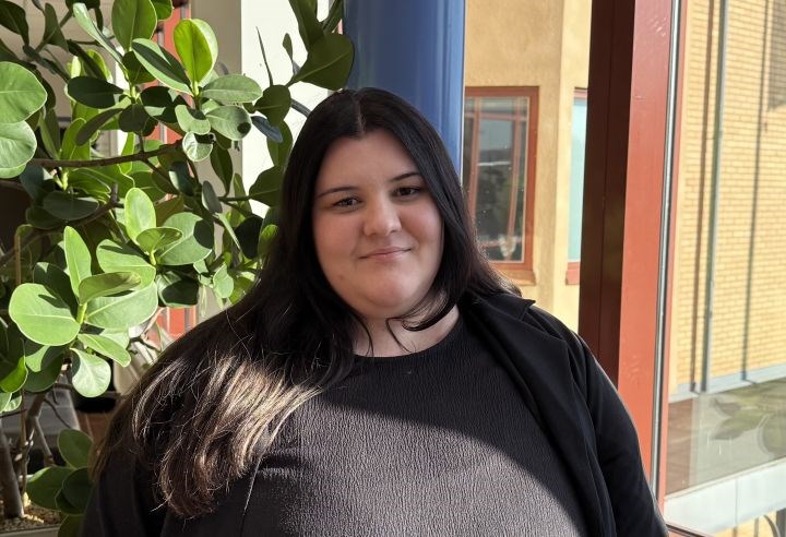 Porträtt av en kvinna i svart tröja med en växt och fönster i bakgrunden