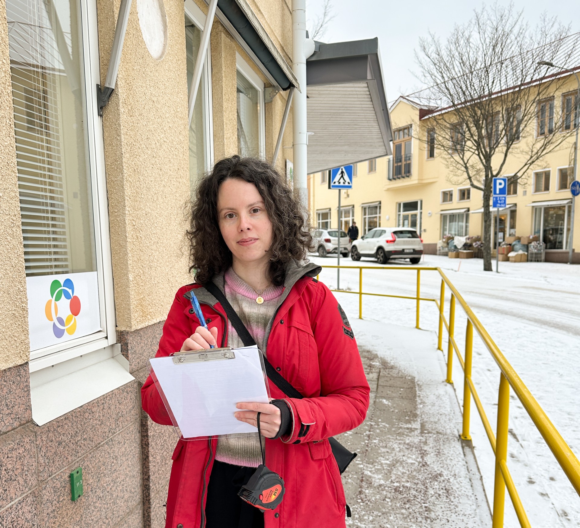 Foto av en kvinna med röd jacka och med en block och en penna i händerna