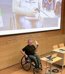 Foto av föreläsare som använder rullstol framför en skärm