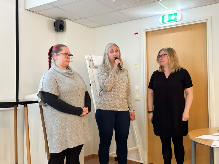 Foto av tre kvinnor, en pratar i mick