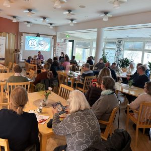 Foto bakifrån visar personer som sitter vid bord på en föreläsning